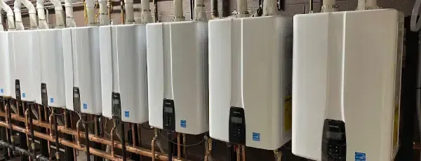 Row of white tankless water heaters. Copper pipes and plumbing visible.