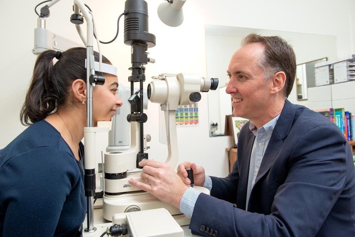 Optometrist examining a patient's eyes with a slit lamp in a clinic.