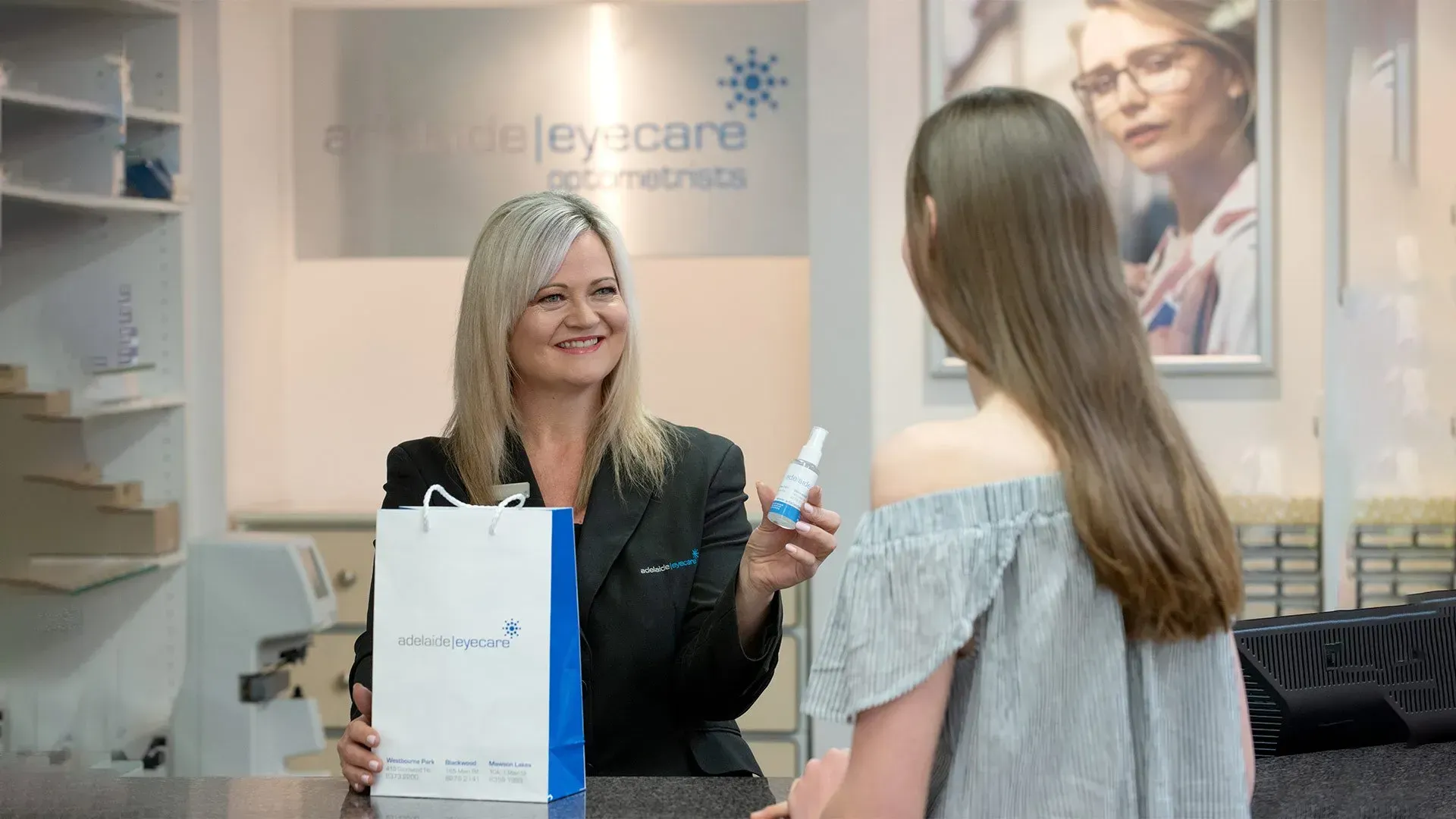 Optometrist hands eye drops and a bag to a customer in a clinic.