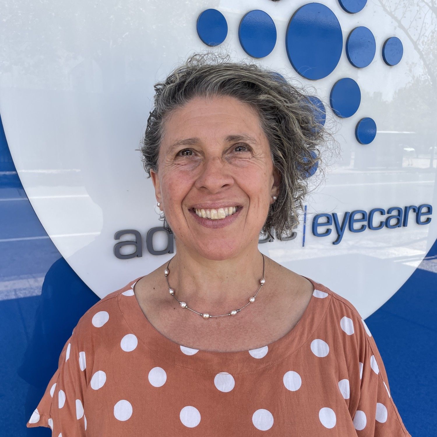 Smiling person standing before an eyecare sign with blue circular logo and white background