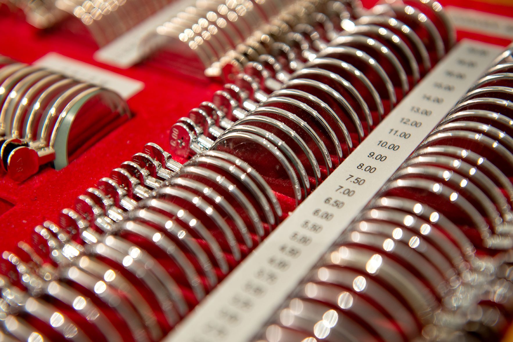 A set of silver-rimmed trial lenses, used in eye exams, arranged in a red case.