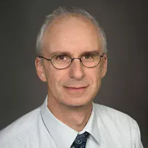 Portrait of a man in glasses, white shirt, and tie against a gray background