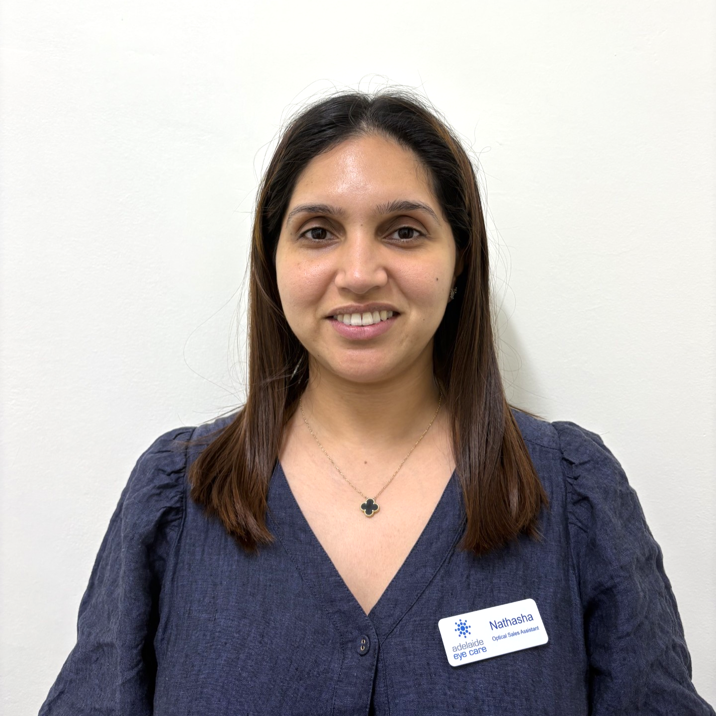 Woman smiling in a navy blouse and name tag against a plain white background