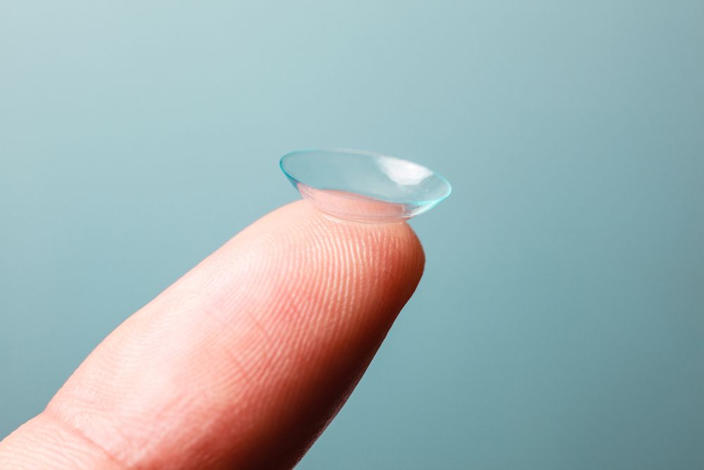 Contact lens on a finger, blue-tinted with a turquoise background.