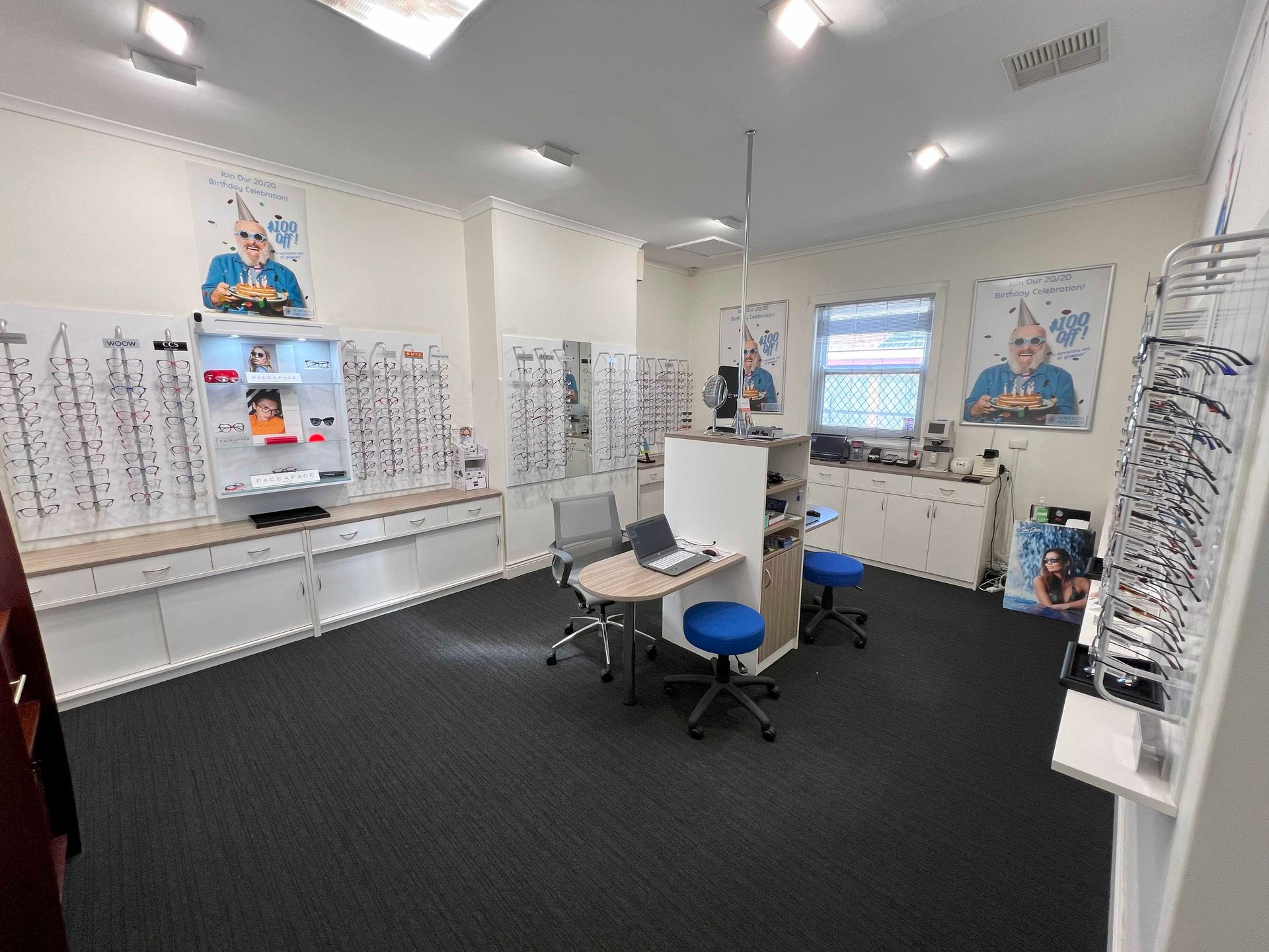 Interior of an optician's shop with eyeglasses displays, examination chairs, and posters on the walls.