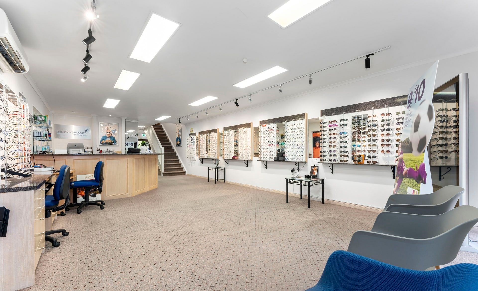 Interior of an optical shop with eyeglasses displays, seating, and a reception desk.