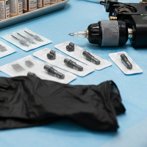 Tattoo machine, needles, and black gloves laid out on a blue surface
