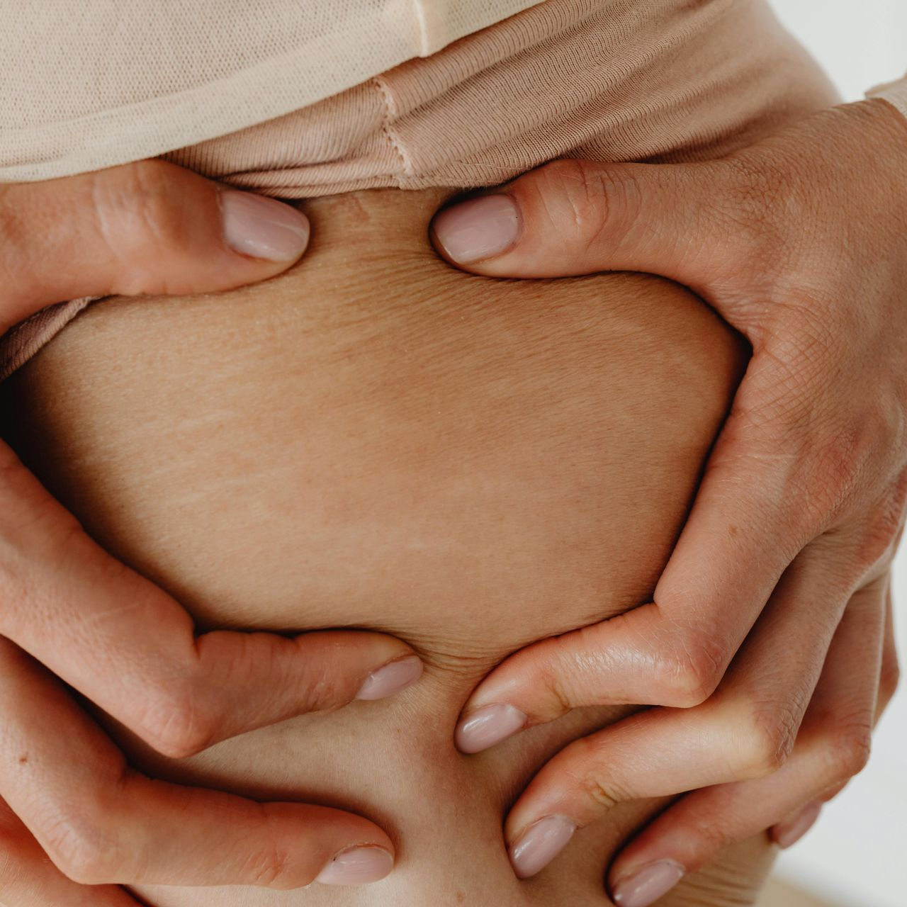 Hands pinching a bare abdomen, forming a heart shape
