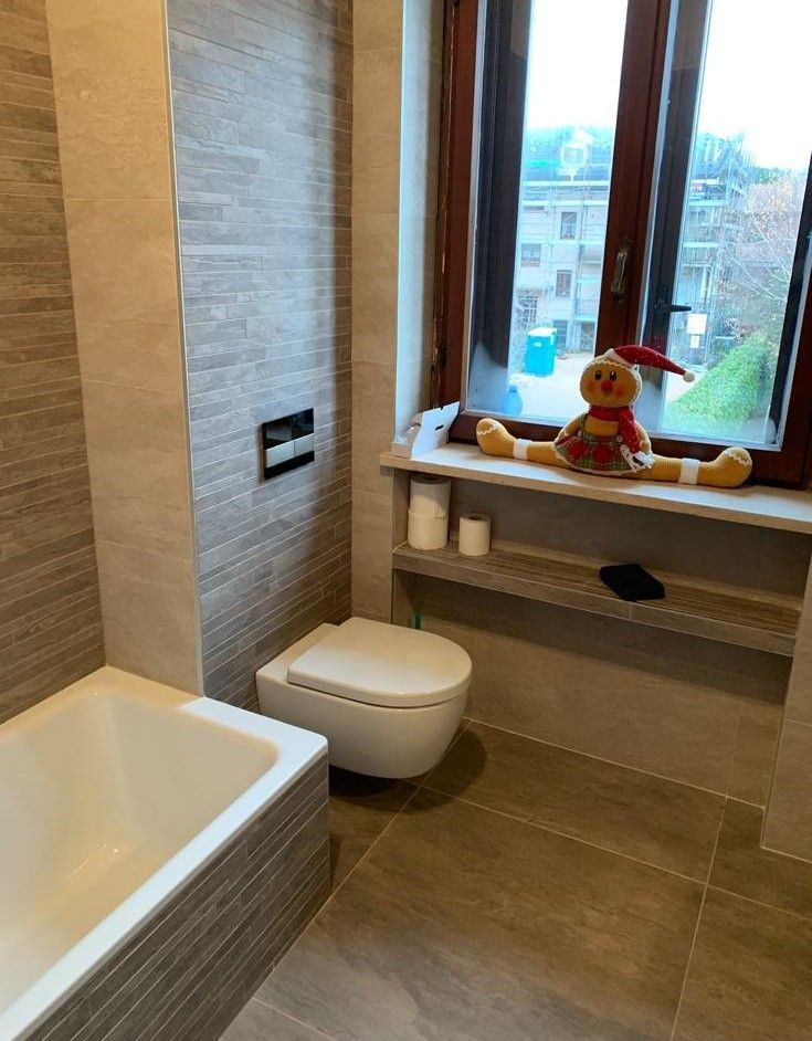 Bagno moderno con vasca da bagno, WC, sedile sotto la finestra e un orsacchiotto di peluche sul davanzale.