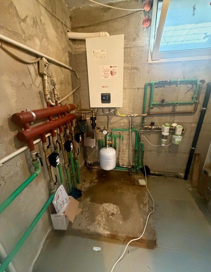 Locale tecnico nel seminterrato con tubature, caldaia, manometri e acqua sul pavimento.