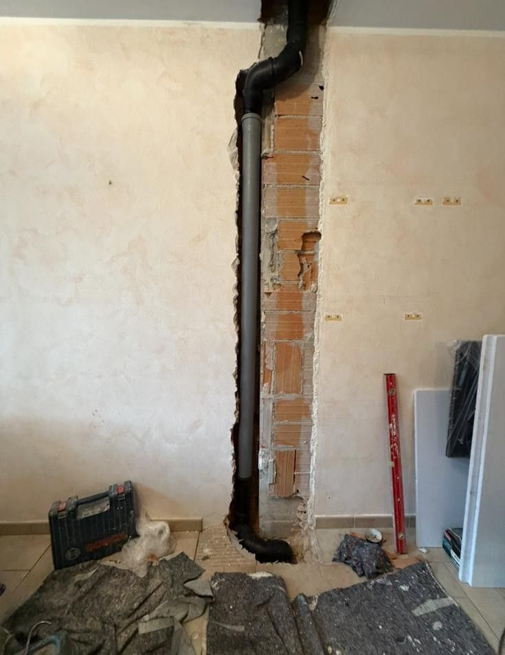 Parete interna con canale verticale in mattoni a vista e tubo nero, circondata da detriti di ristrutturazione.