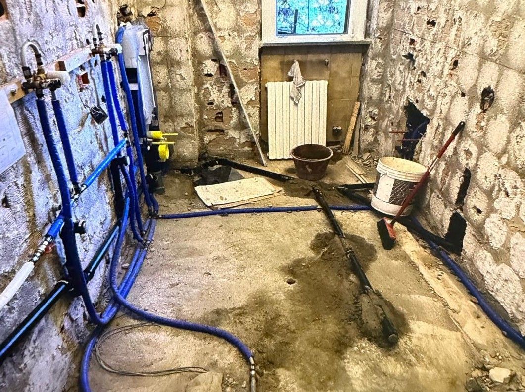 Locale tecnico nel seminterrato con tubi flessibili blu, condotti e uno scarico su un pavimento di cemento bagnato.