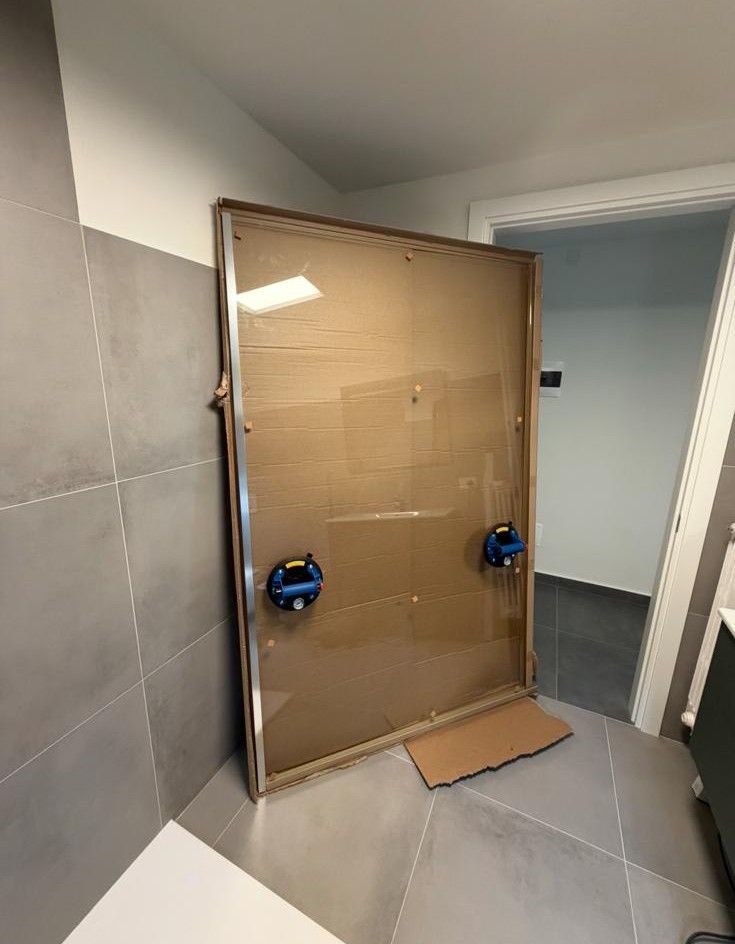 Ampio box doccia in vetro con maniglie blu in un bagno piastrellato in fase di ristrutturazione.