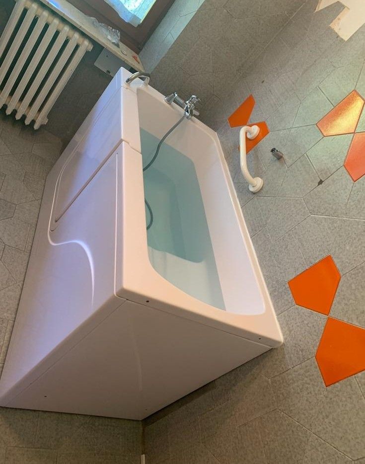 Vasca da bagno bianca in un bagno piastrellato con dettagli arancioni sul pavimento e un termosifone nelle vicinanze.
