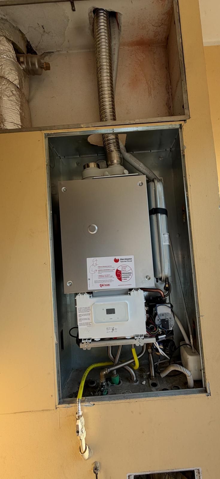 Quadro elettrico a vista in una parete gialla, con cavi e condotti a vista nella parte superiore.