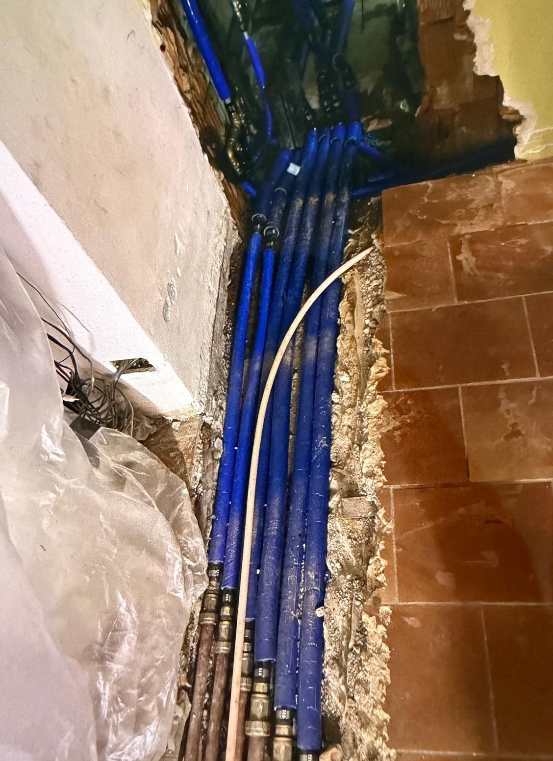 Cavi blu che corrono lungo una parete fino a un pavimento piastrellato, con un angolo danneggiato e detriti di costruzione.