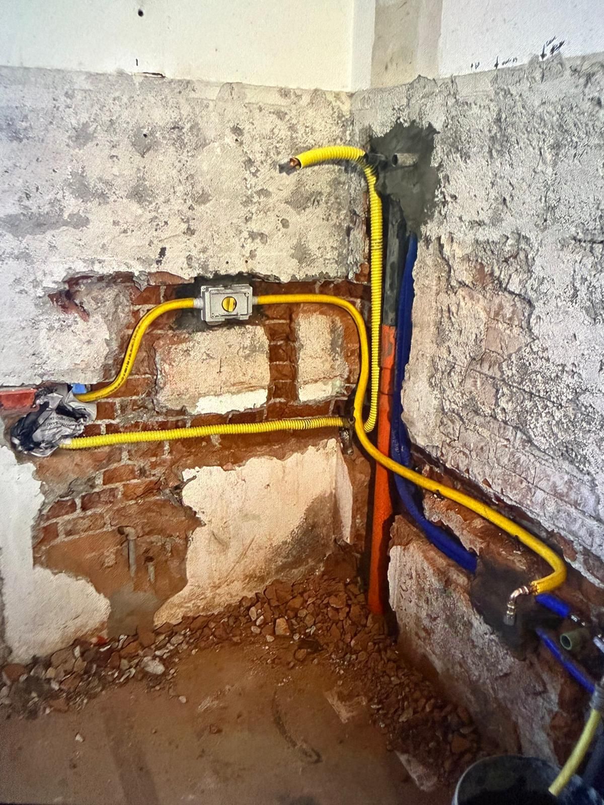 Tubature elettriche e idrauliche gialle e blu a vista su una parete grezza e non rifinita durante i lavori di ristrutturazione.