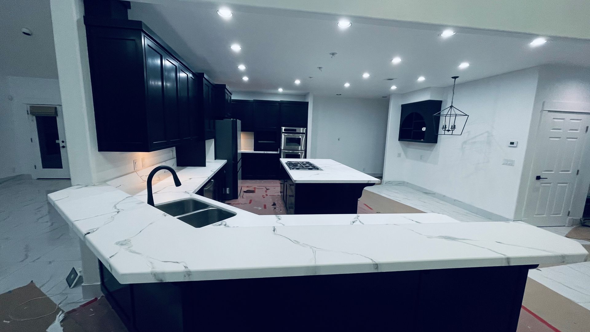Modern black kitchen with white countertops and island, with multiple recessed lights.