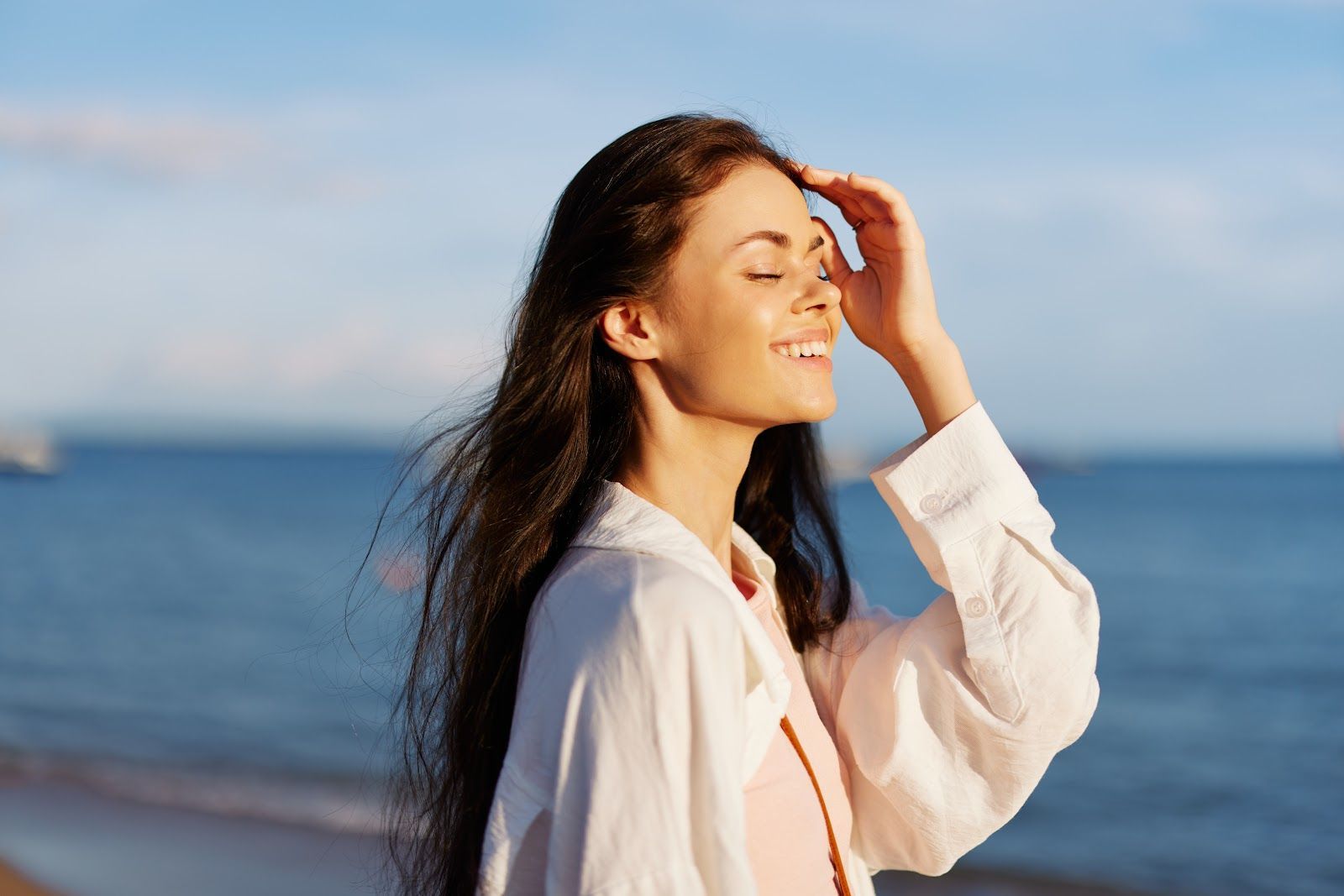 Woman in a white shirt smiling by the sea with wind in her hair