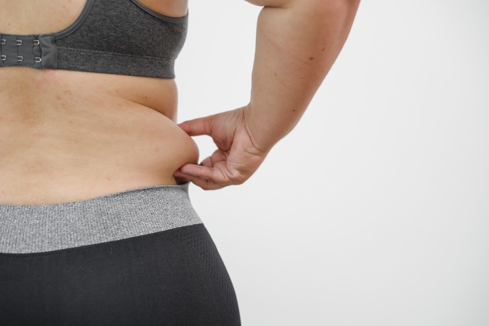 Person pinching side waist fat in gray sportswear against a white background
