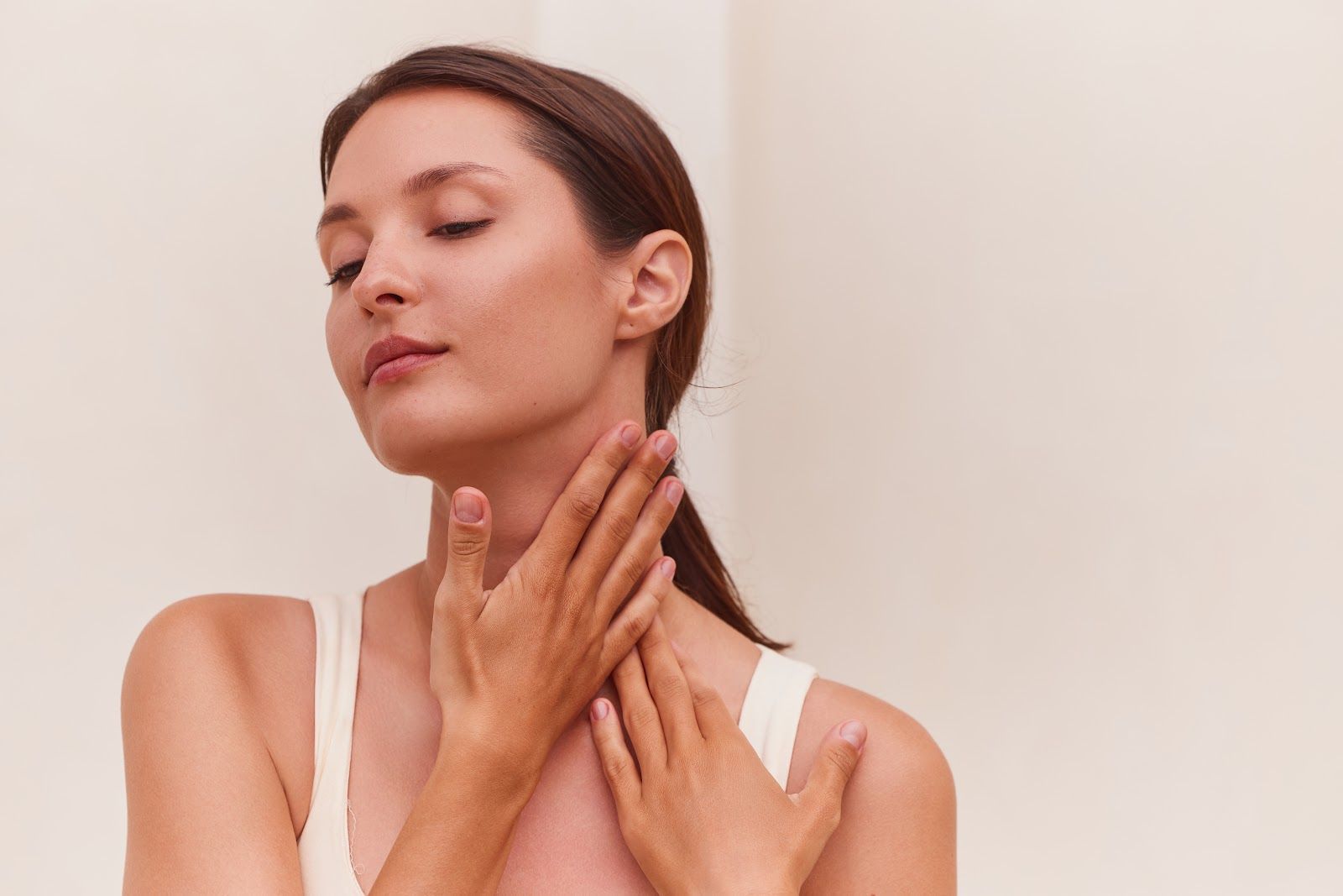 Woman applying skincare to her neck against a plain beige background