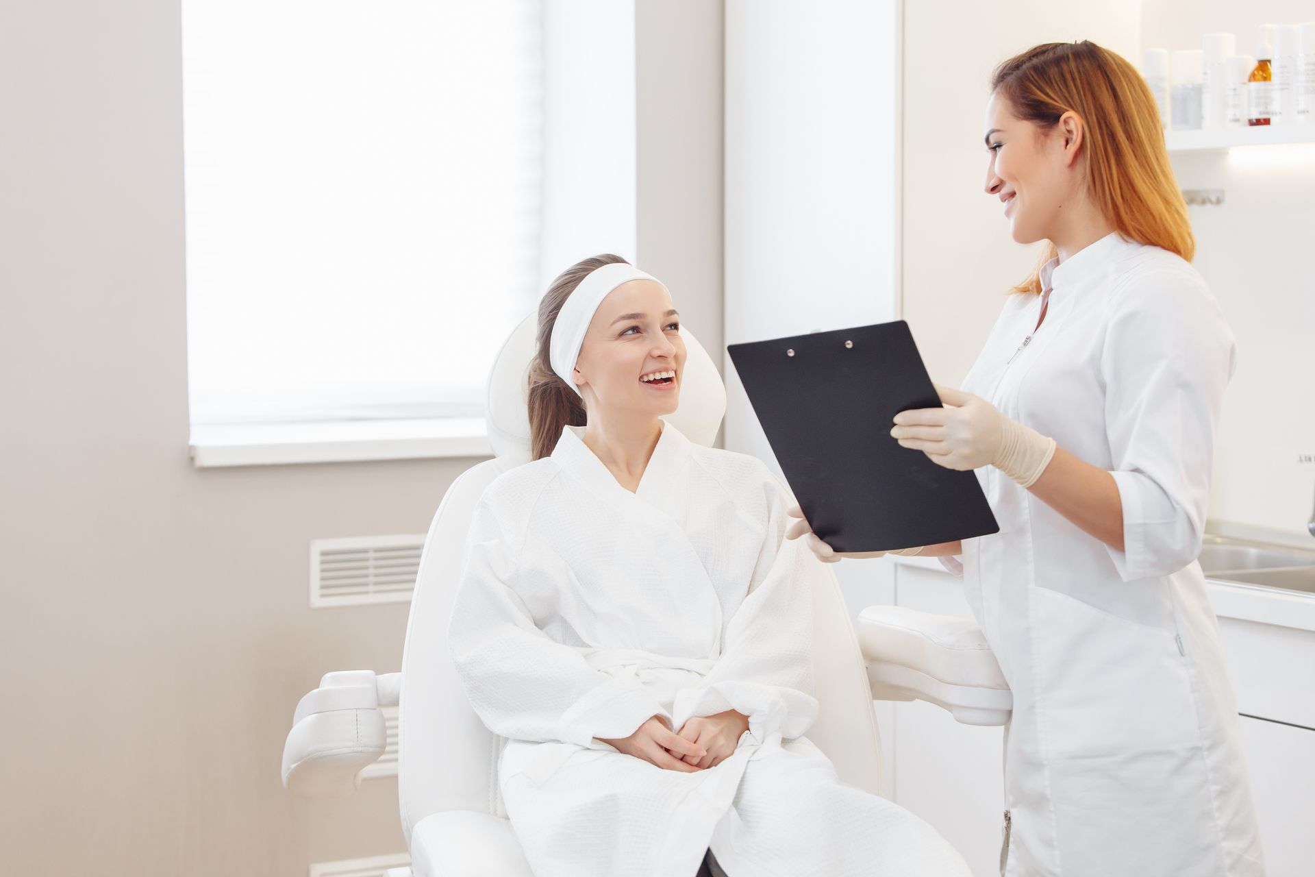 Patient smiling in a white robe while a clinician reviews notes in a bright exam room