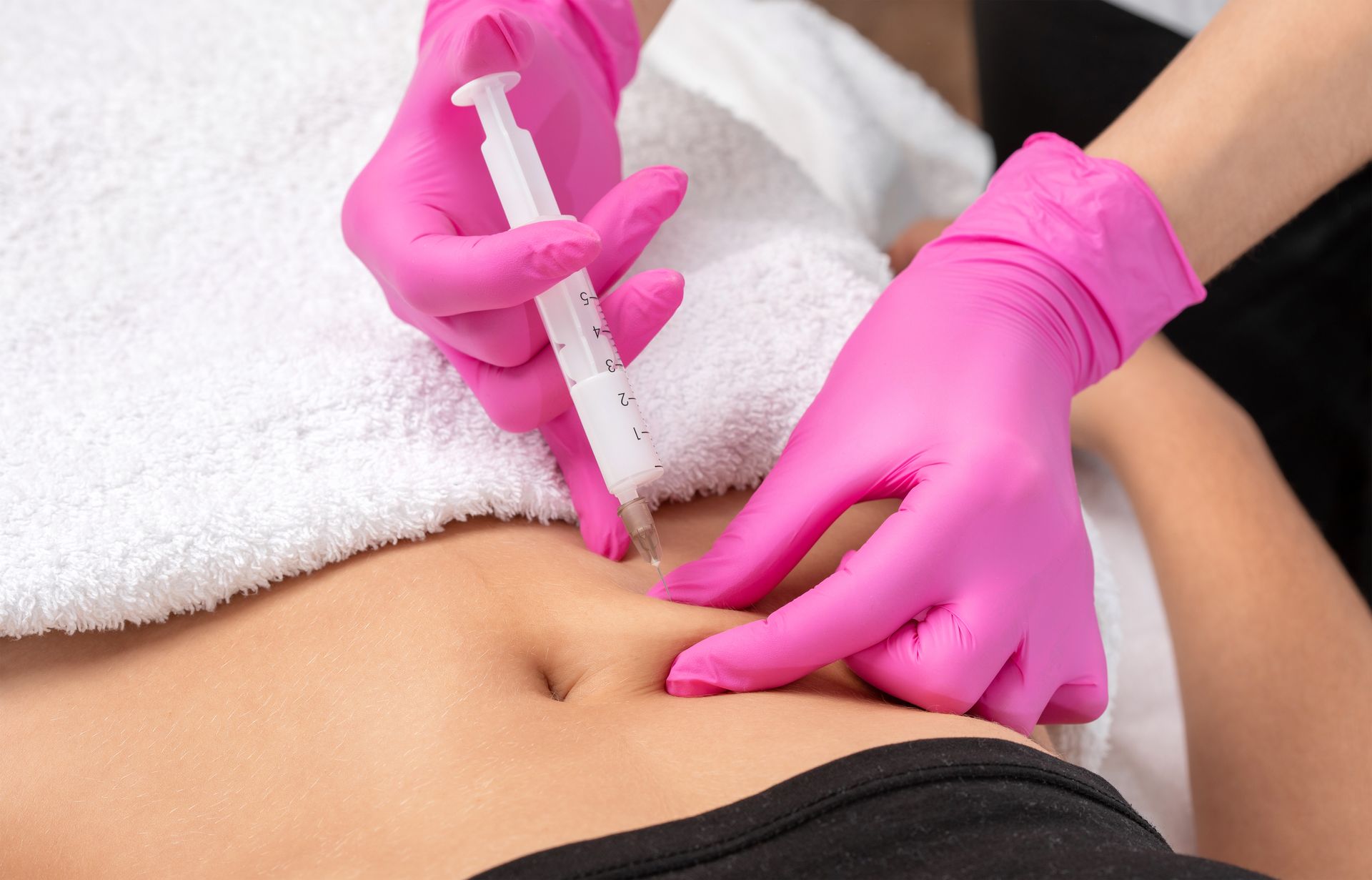 Gloved hands injecting a syringe into a person’s abdomen during a cosmetic treatment