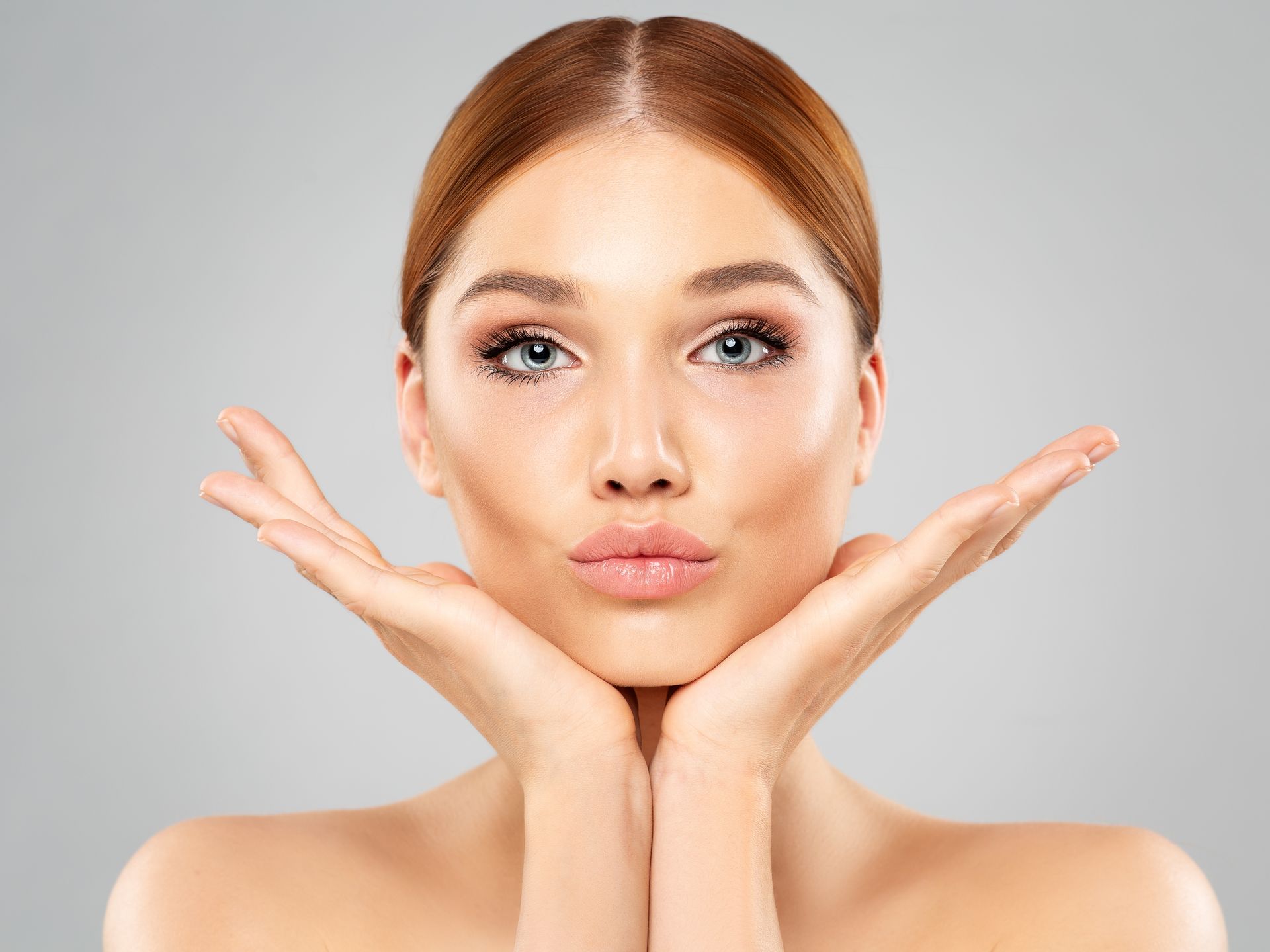 Woman with light skin, rosy cheeks, and pursed lips poses with hands framing her face.