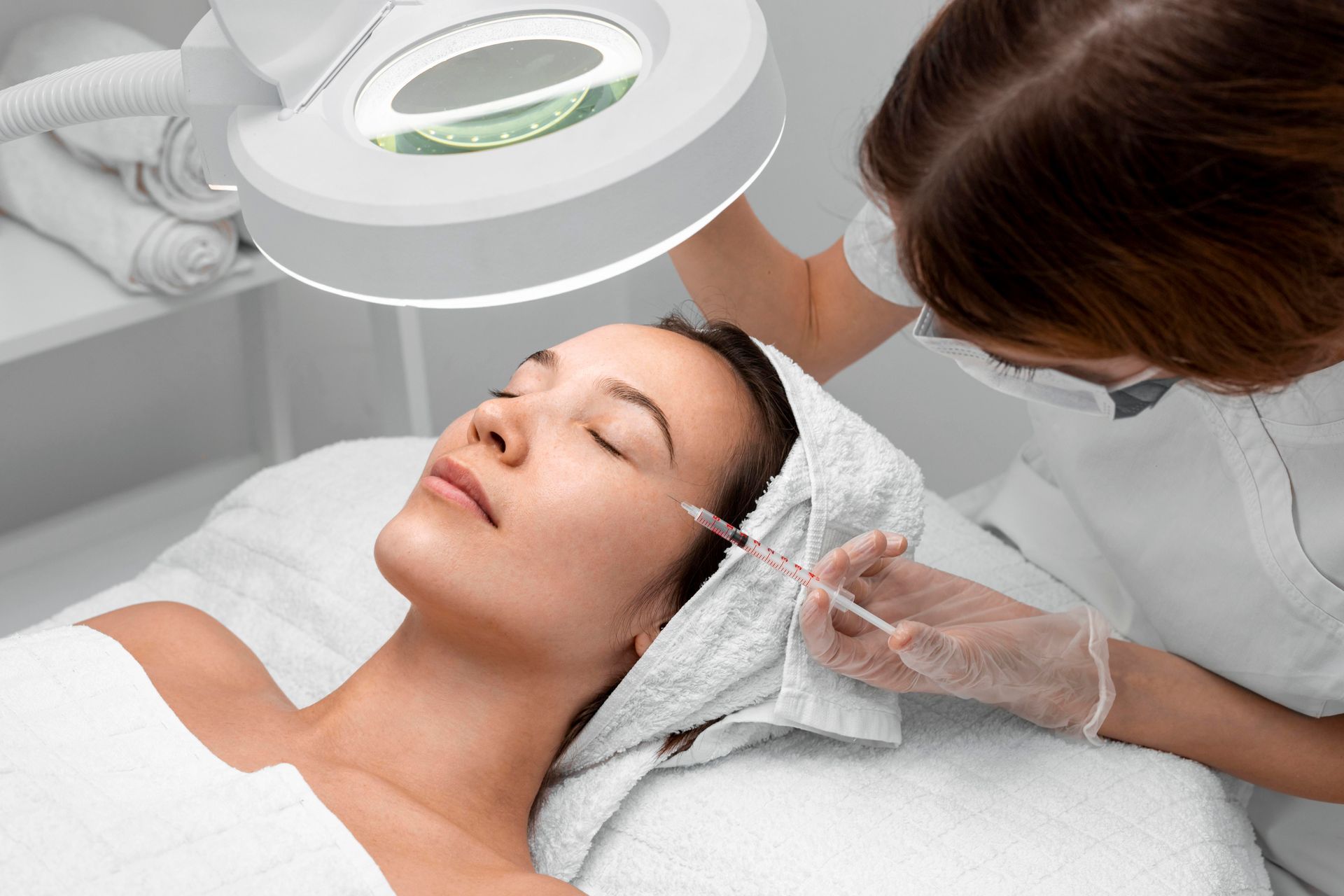 Cosmetic facial treatment with a magnifying lamp as a clinician applies a tool near the client’s cheek