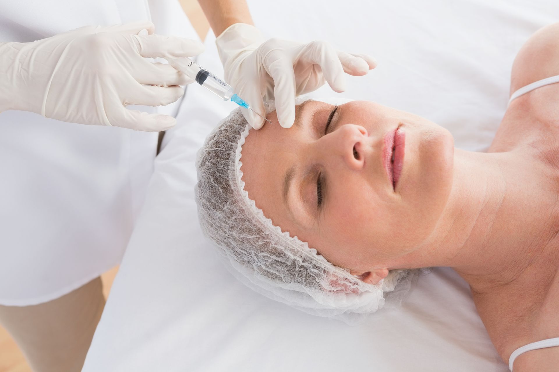Aesthetic facial treatment with gloved hands applying serum to a client’s forehead