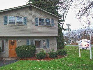 Two-story tan building with teal shutters, a brown door, and a sign for