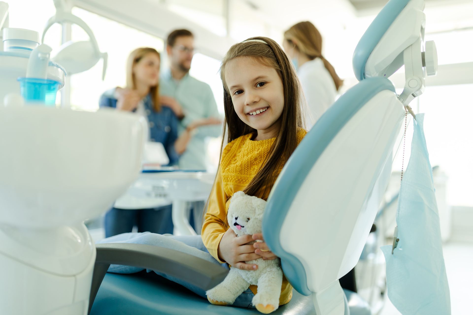 Little girl showing milk tooth, parent discussing with dentist, showcasing family dentist care.