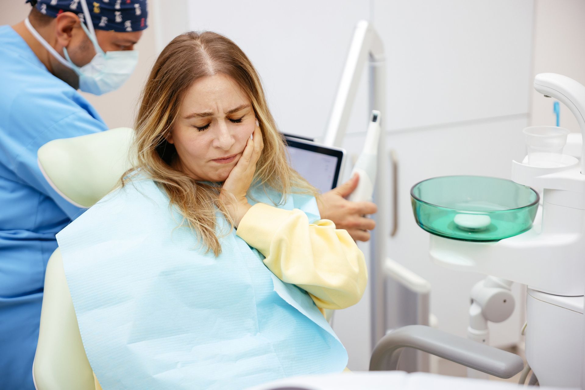 A dental patient sitting in a clinic chair wearing a bib while her dentist explains a treatment