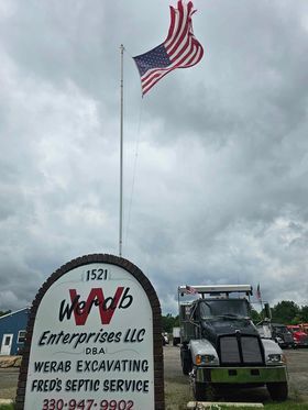 A truck is parked in front of a sign with an american flag flying in the background