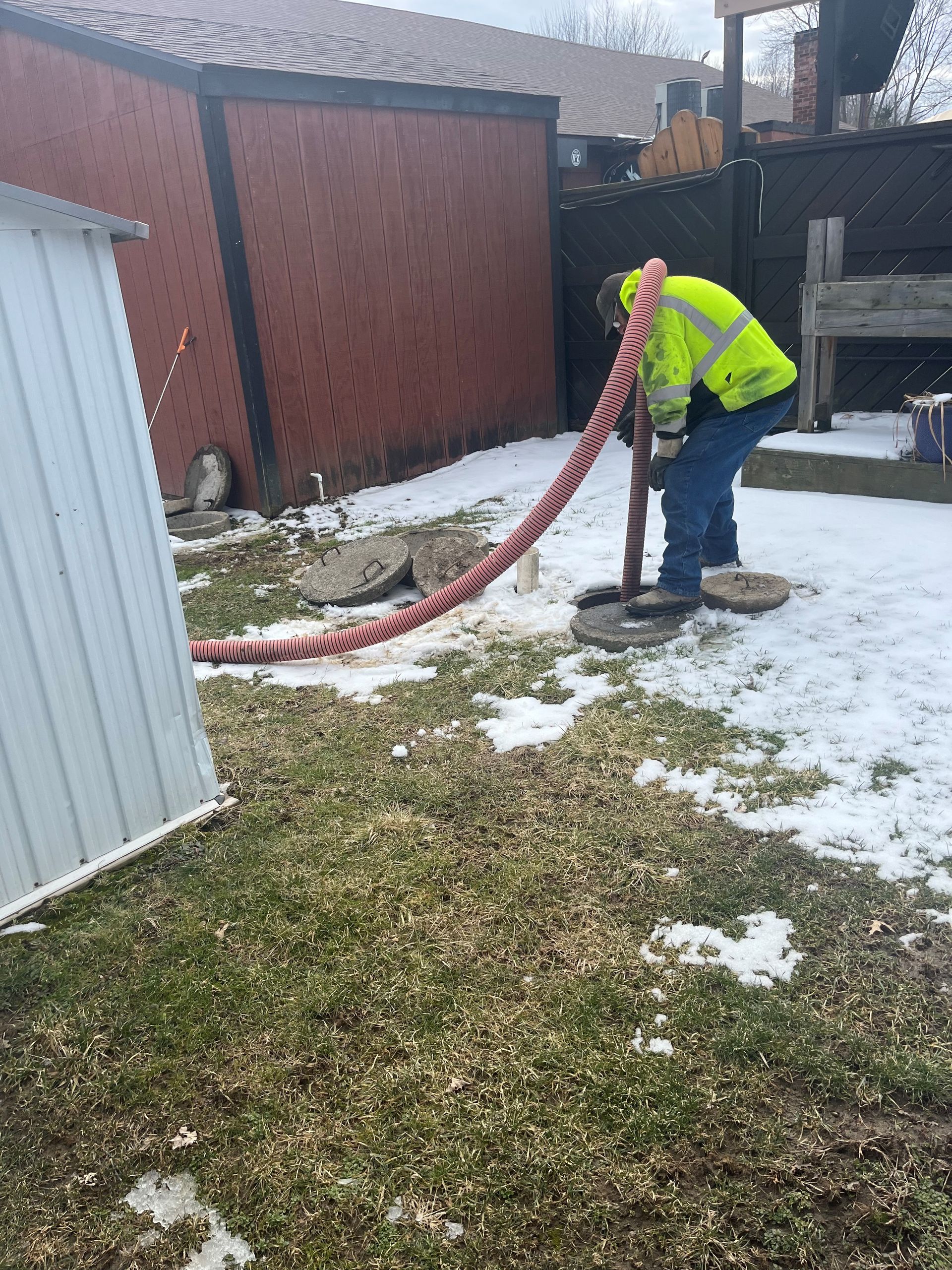A man is pumping water into a septic tank with a hose.