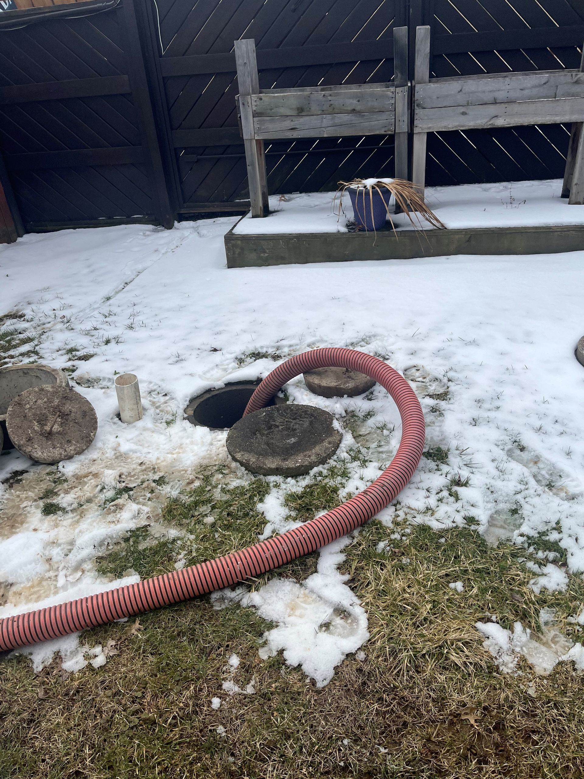 A red hose is connected to a drain in the snow.