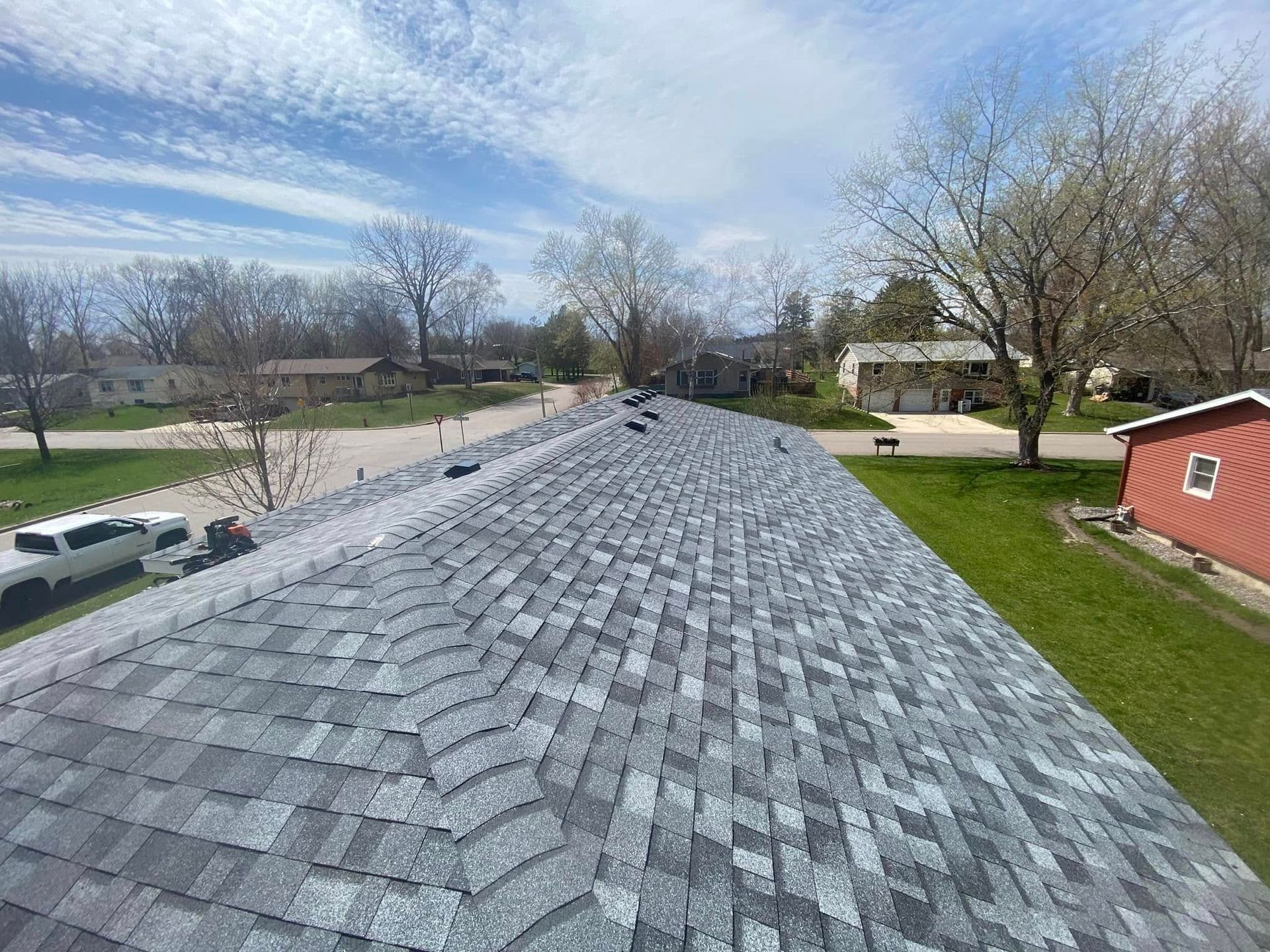 Gray shingle roof under a blue sky, viewed from above in a suburban neighborhood
