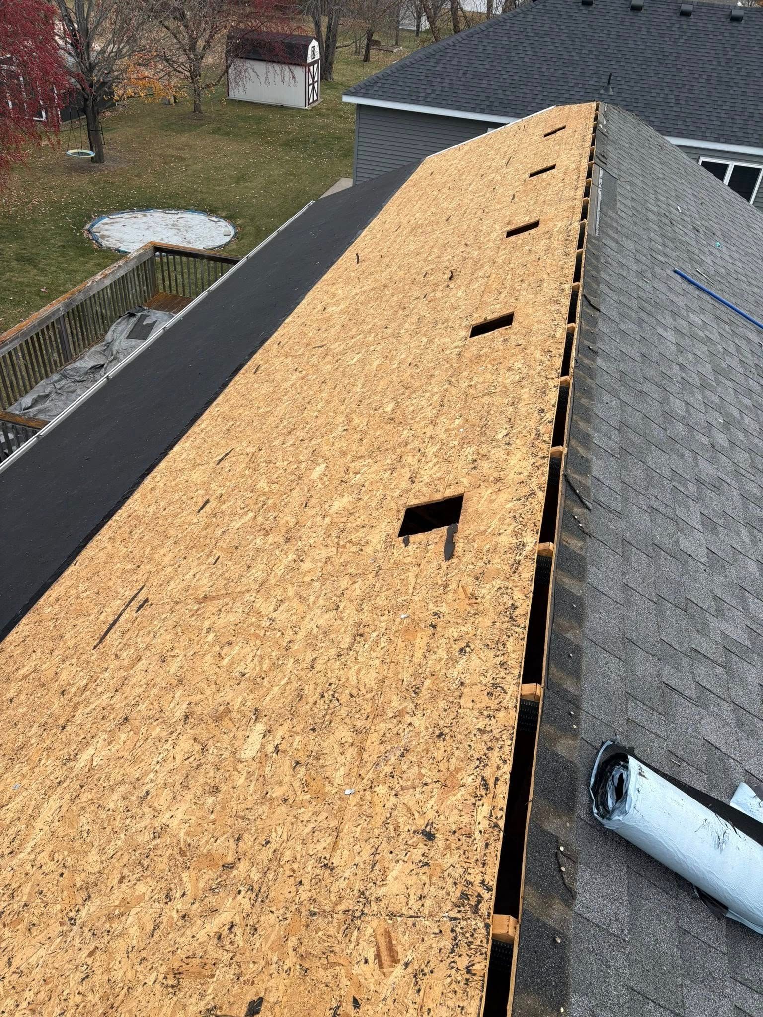Roof under repair with plywood sheathing exposed beside gray shingles