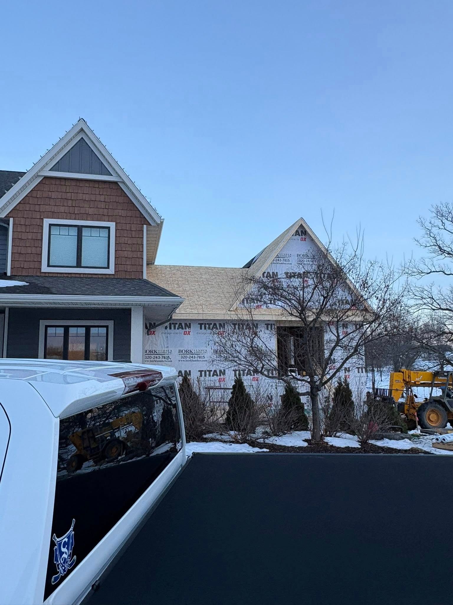 Snow-covered suburban house with brick and white siding, a driveway, and a yellow snowblower on the right