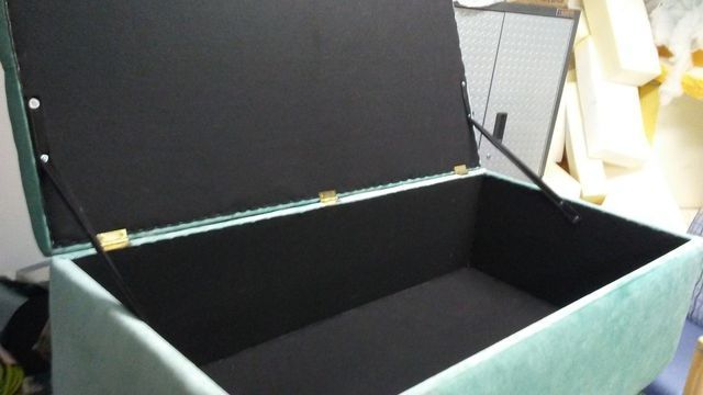 A green ottoman with the lid open is sitting on a table.