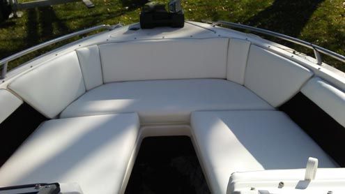 The front of a white boat with white cushions and a tree in the background.