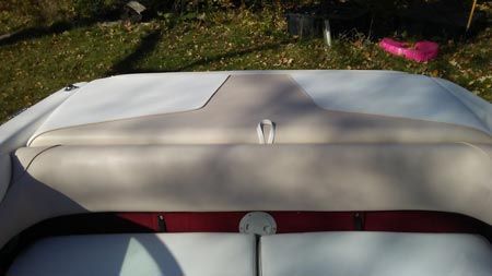 The back of a white and red boat is sitting in the grass.