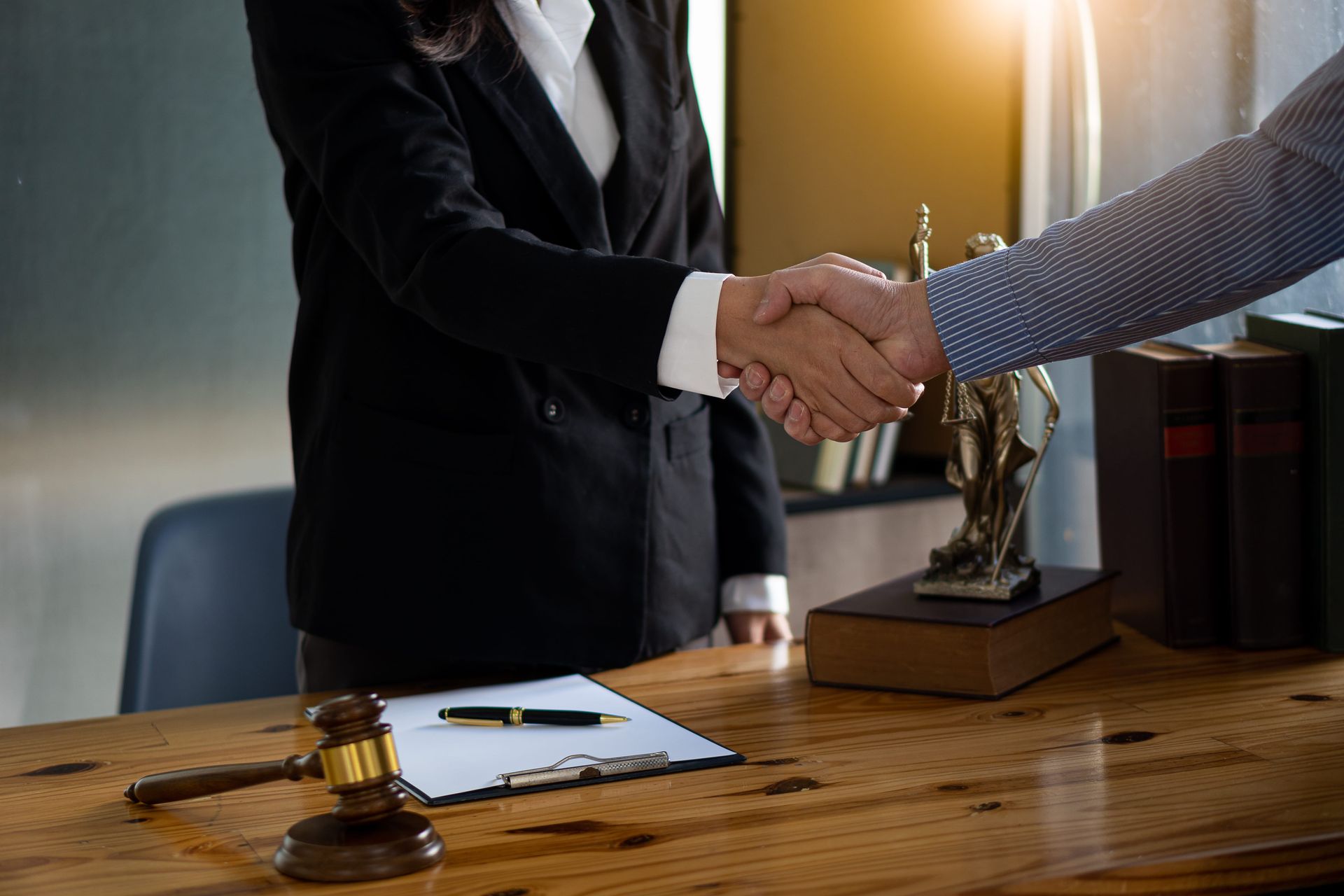 Two people shaking hands across a wooden desk in a law office