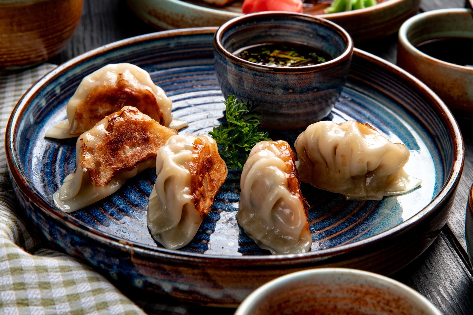 Dumplings on a blue-rimmed plate with dipping sauce and tea on a tablecloth