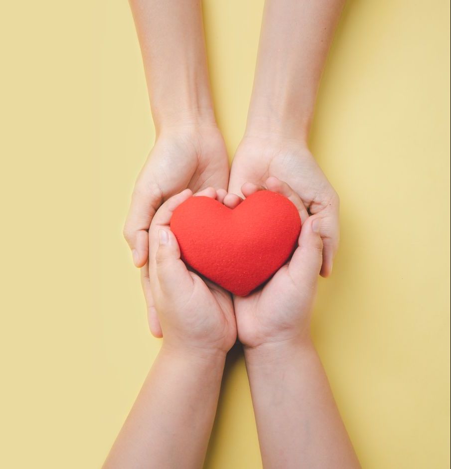 Hands cradling a red heart on a yellow background.