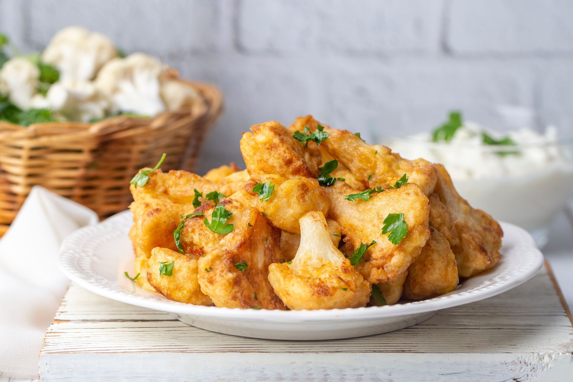 Plate of golden fried cauliflower garnished with parsley on a rustic table