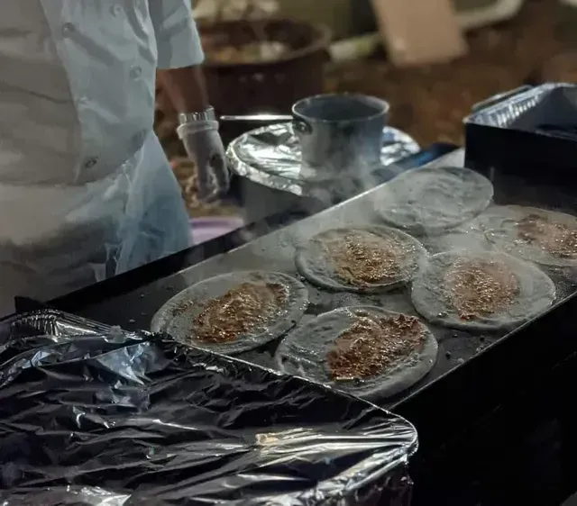 Cook plating flatbreads on a griddle as steam rises in a busy kitchen