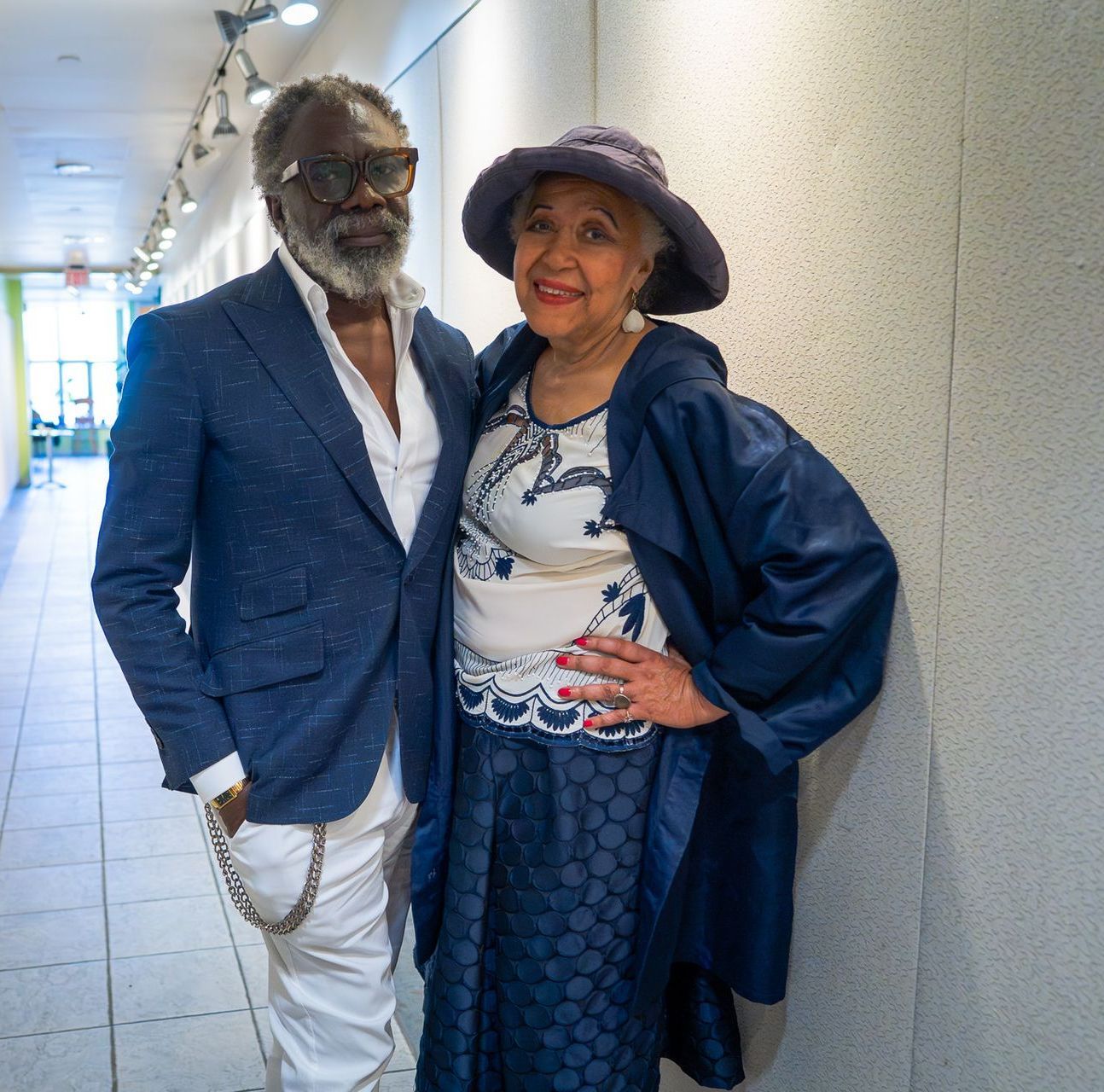 Two people posing in a hallway, wearing coordinated blue outfits and smiling