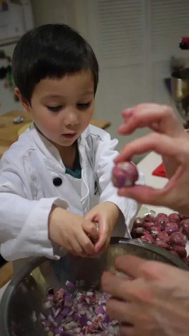 Child helping peel purple grapes in a kitchen with an adult’s hands nearby