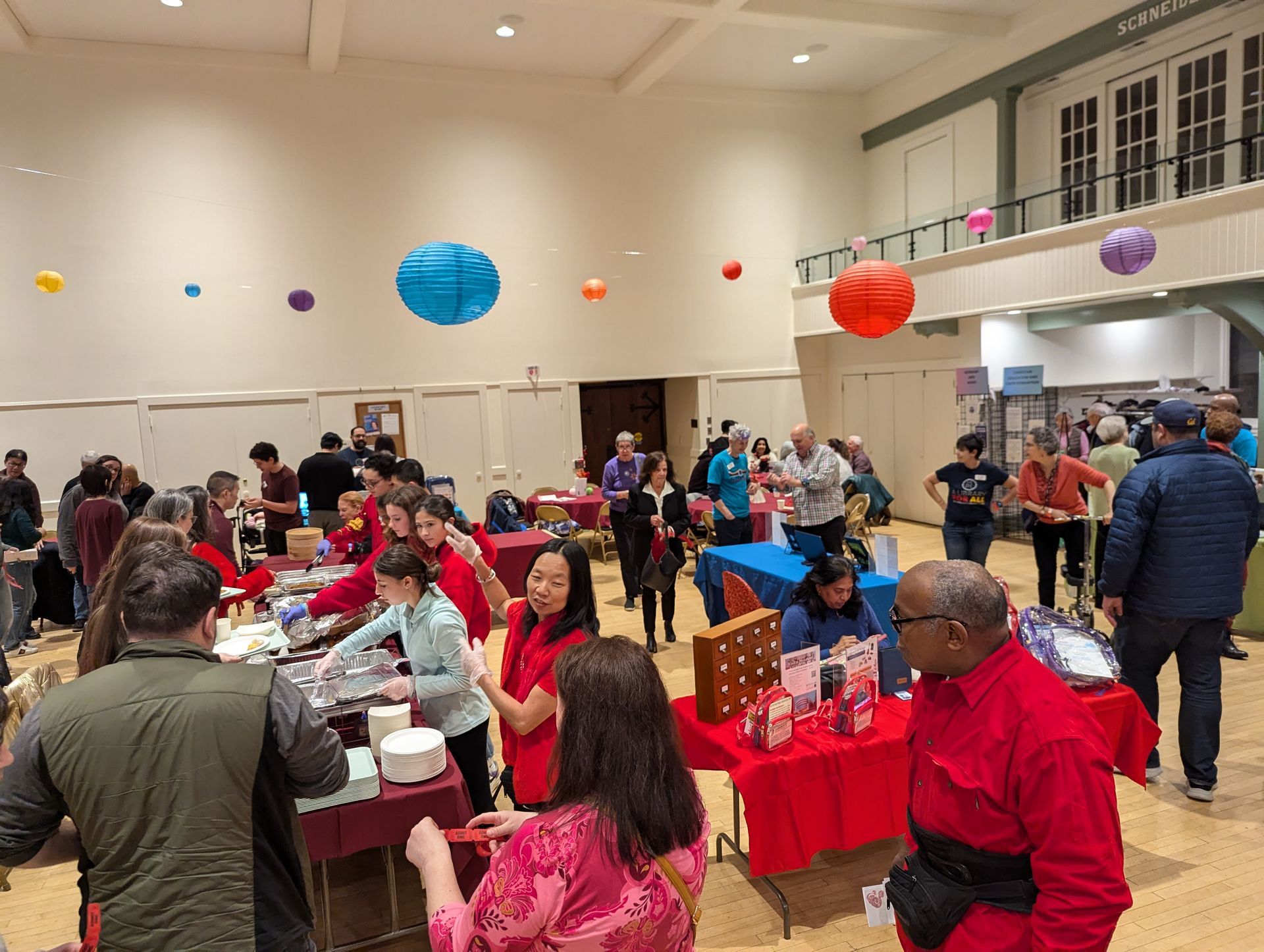 Crowded indoor fair with vendor tables, red decorations, and people browsing in a bright hall